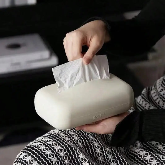 Person holding a beige tissue box with a white tissue being pulled out, in a car interior.