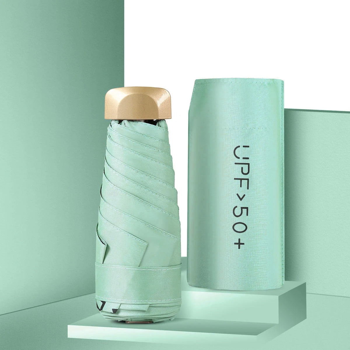 Foldable mint green umbrella with gold cap and cylindrical case on a light green background