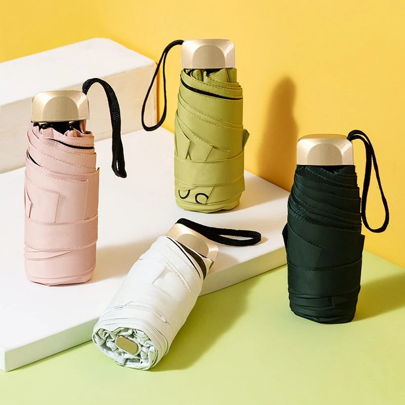 Four folded umbrellas in pink, green, white, and black on a yellow background