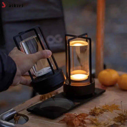 Hand holding a black lantern with another lantern in the background on a wooden surface.