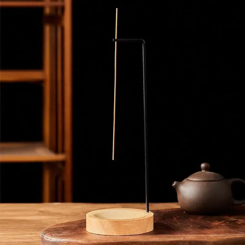 Incense stick holder on a wooden surface with a teapot in the background