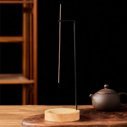 Incense stick holder on a wooden surface with a teapot in the background
